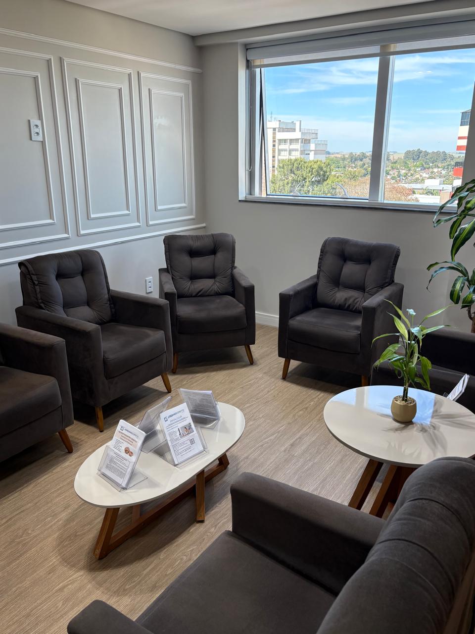 Sala de espera da clínica, com poltronas escuras, mesas claras e janela ampla.
